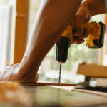 Un homme utilise une perceuse, un des nombreux outils de construction, pour percer une planche de bois en intérieur