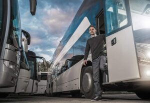 Un chauffeur professionnel descend d'un grand bus de voyage blanc garé sur un parking avec d'autres véhicules, illustrant comment choisir le bon autocar pour son groupe.
