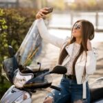 Femme prenant un selfie sur un scooter équipé d’un pare-brise moto lors d’une journée ensoleillée.
