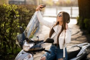 Femme prenant un selfie sur un scooter équipé d’un pare-brise moto lors d’une journée ensoleillée.