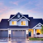 Une maison à deux étages avec garage, fenêtres éclairées, pelouse et ciel crépusculaire